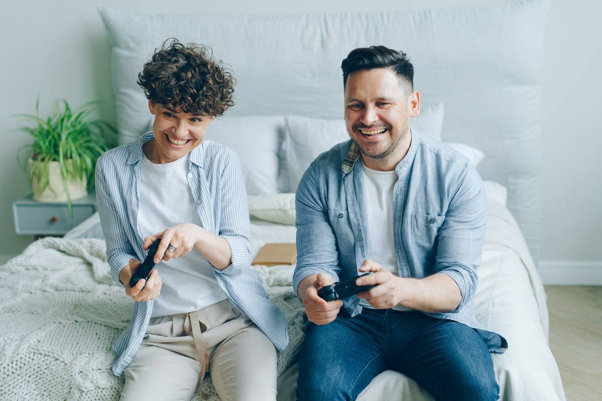 Cute couple boyfriend and girlfriend playing videogame sitting on bed in bedroom
